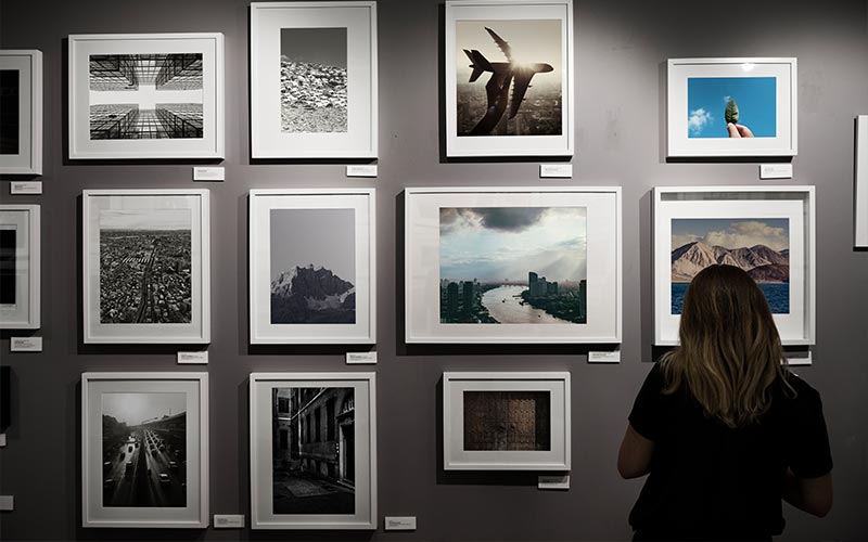 A female photography enthusiast looking at the pictures hanging on the wall in an exhibition