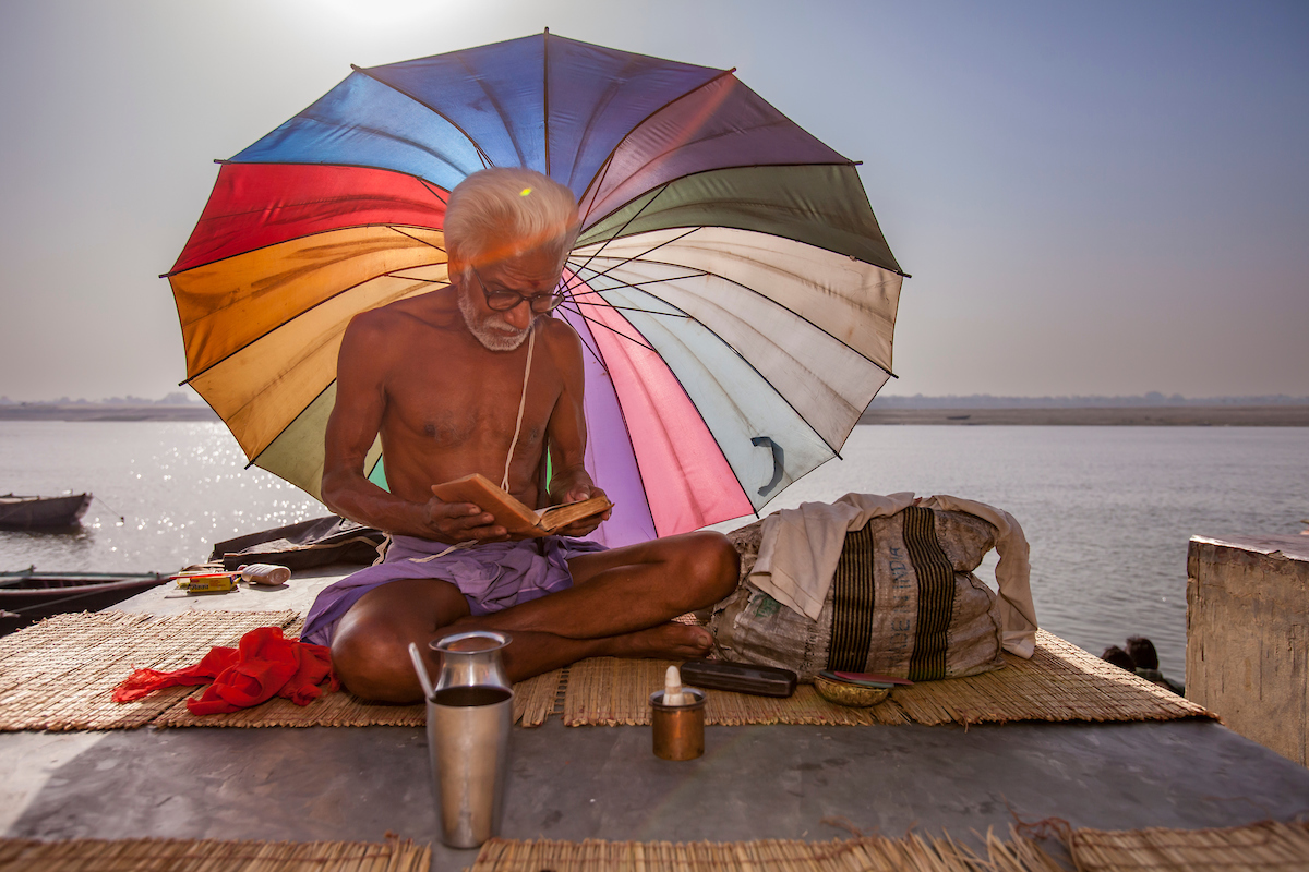An image of aman studying Hindu scriptures under the umbrella