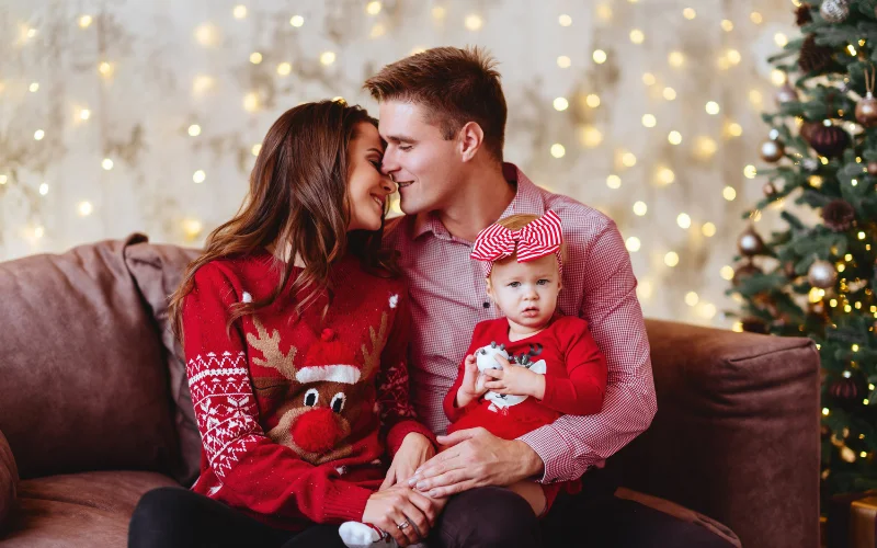 a couple posing in Christmas sweaters with their baby