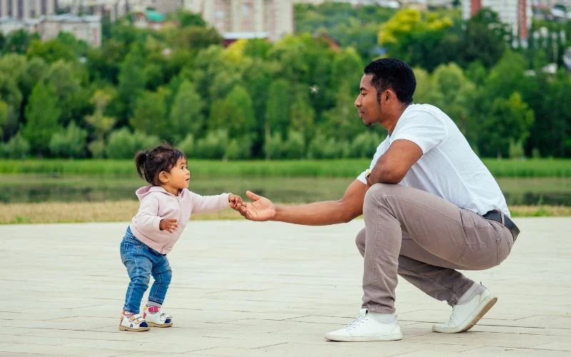 baby taking steps while her dad holds her hands