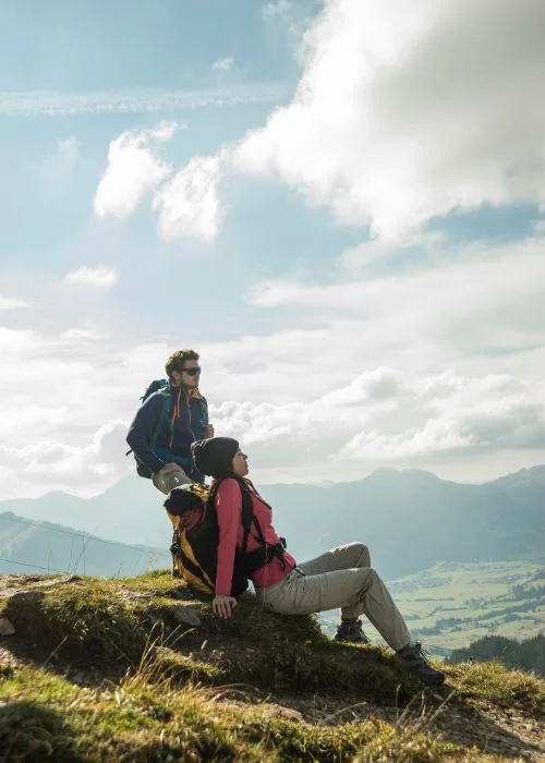 Two hikers resting on a mountain viewpoint while enjoying a scenic landscape, creating a natural hiking portrait photography moment.