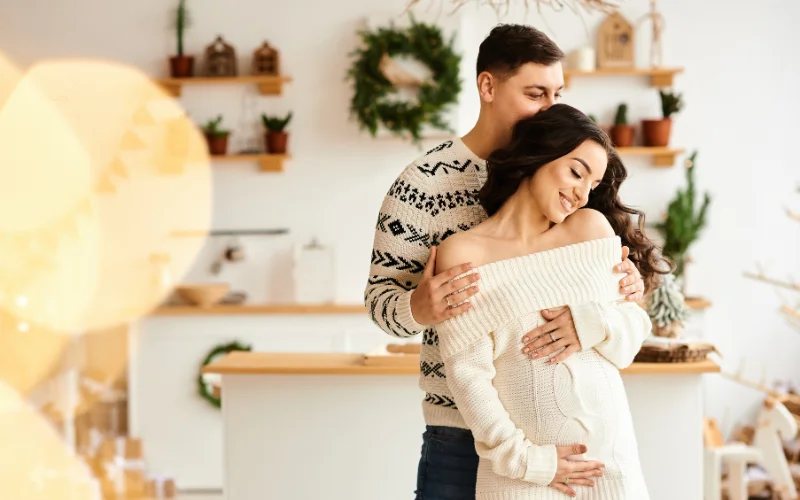 a pregnant woman and her husband posing wearing all white - Christmas pregnancy photo ideas