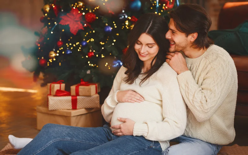 pregnant woman and husband sitting next to the Christmas tree