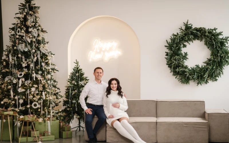 a couple posing on a sofa next to the Christmas tree